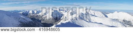 Breathtaking Panoramic Shot Of Mountain Peaks Covered In Snow During The Winter Season. A Blue Sky W