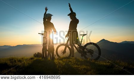 Two Happy Woman High Five Over The Sunset After A Successful Mountain Biking Trip In The Mountains. 