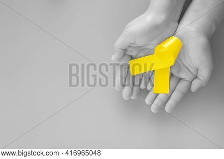 Hand Holding Yellow Ribbon On Black And White Background, Copy Space. Bone Cancer Sarcoma Awareness 