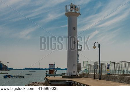 Pyeongtaek, South Korea; April 6, 2021: White Lighthouse On End Of Concrete Pier Under Blue Sky With