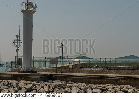 Pyeongtaek, South Korea; April 6, 2021: White Lighthouse On End Of Concrete Pier Under Gray Overcast