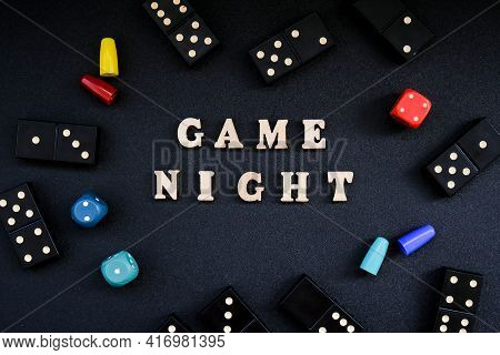 Text Game Night Spelled Out In Wooden Letter. Surrounded By Dice, Dominoes Other Game Pieces On Blac