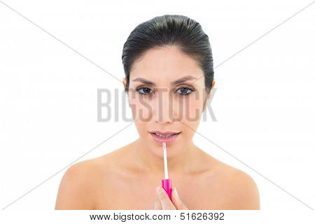 Brunette applying lip gloss and looking at camera on white background