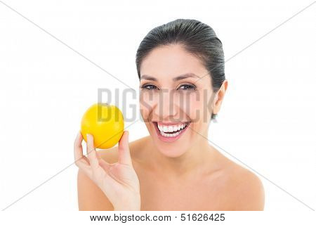 Smiling brunette holding an orange and looking at camera on white background