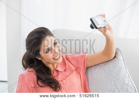 Brunette sitting on her sofa taking a picture of herself at home in the sitting room