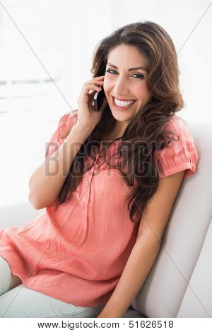 Pretty brunette sitting on her couch on a phone call at home in the living room