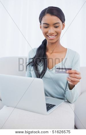 Cheerful attractive woman in bright living room using her laptop to buy online