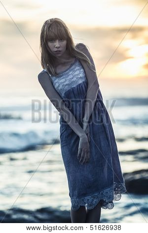 Beautiful young model standing on rocks by the sea on a glowing background