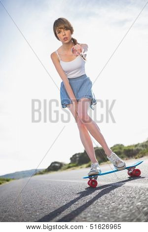 Young woman pointing at camera while balancing on her skateboard on a deserted road