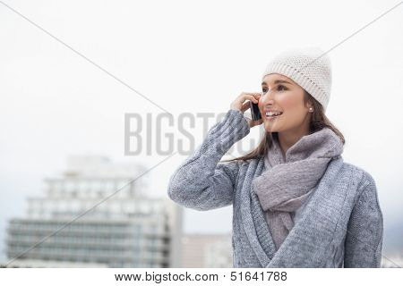 Relaxed brunette with winter clothes on having a call outdoors on a cold grey day