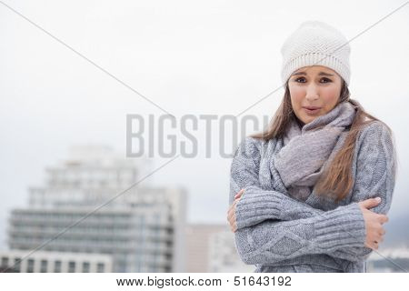 Shivering cute brunette with winter clothes on posing outdoors on a cold grey day