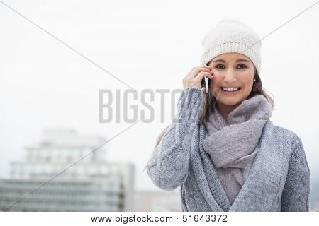 Smiling woman with winter clothes on having a call outdoors on a cold grey day