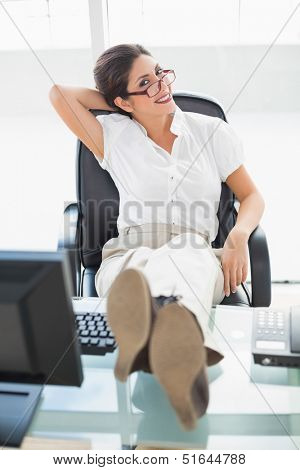 Relaxed businesswoman sitting at her desk with her feet up smiling at camera in her office