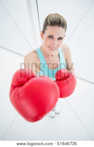 Smiling fit woman wearing red boxing gloves in bright fitness studio