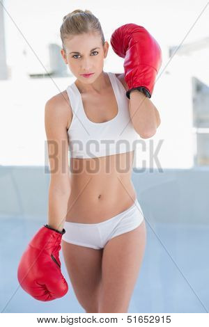 Severe young blonde model in white sportswear wearing boxing gloves