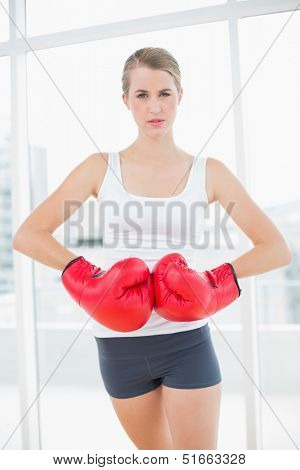 Competitive woman with red boxing gloves posing in bright sports hall