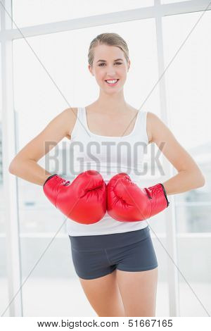 Smiling competitive woman with red boxing gloves posing in bright sports hall