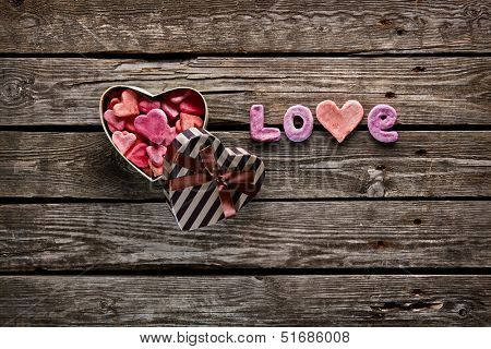 Open heart shaped Valentines Day gift box with heap of small hearts inside and word love on old wooden background.