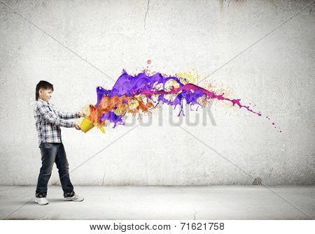 Young boy splashing colorful paint from bucket