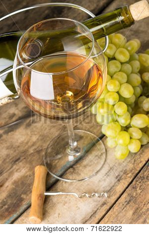 Wineglass With White Wine, Botlle, Corkscrew And Cluster Of Grapes Around On Wood Background
