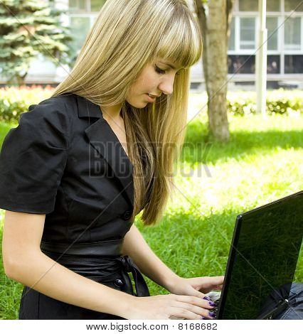 Pige i sort, på plænen med en bærbar computer