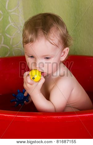 Beautiful little blond girl sitting in the bathroom and chew toys