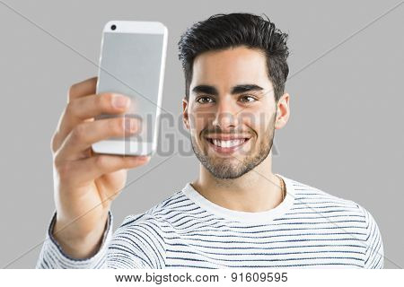 Handsome young man making a selfie picture with phone, isolated over gray background