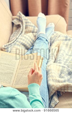 Young woman reading book, close-up, on home interior background