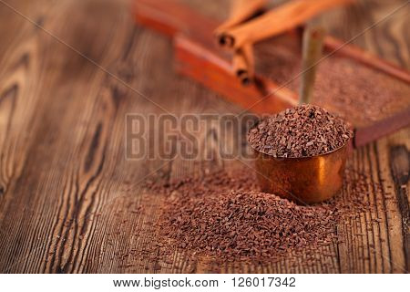 grated dark chocolate in copper measure pan on wooden background