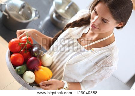 Smiling young woman holding vegetables standing in kitchen