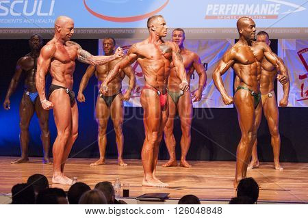 MAASTRICHT THE NETHERLANDS - OCTOBER 25 2015: Male bodybuilders flex their muscles and show their best physique in a side pose on stage at the World Grandprix Bodybuilding and Fitness of the WBBF-WFF