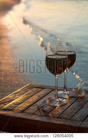 Romantic beach scene: two glasses of red wine at sunset near water line