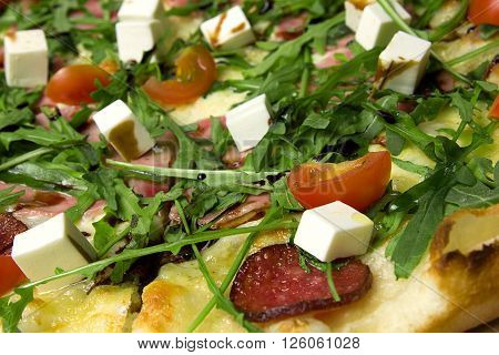 Appetizing pizza with ham, salami, arugula, cherry tomatoes, fetaksa, balsamic closeup