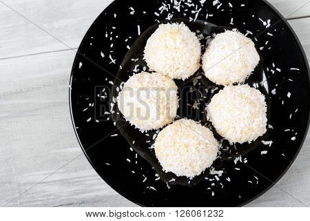 Homemade DIY natural vegan healthy millet gruel and coconut pralines with coconut oil and almond aromate - Rafaello style on a black plate and wooden table. Organic product.