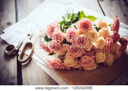 Florist's workspace: bouquet of fresh roses and scissors on an old vintage wooden board table.