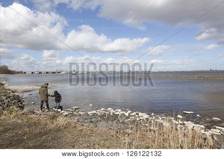 Naarden, netherlands, 6 april 2016: mother and child on stony shore and cloudscape above lake Gooimeer in the netherlands with Hollandse brug in the background