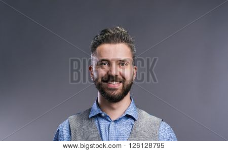 Hipster businessman in blue shirt and gray vest, studio shot on gray background