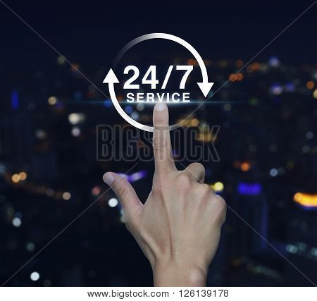 Hand pressing button 24 hours service icon over blurred light city tower background Full time service concept