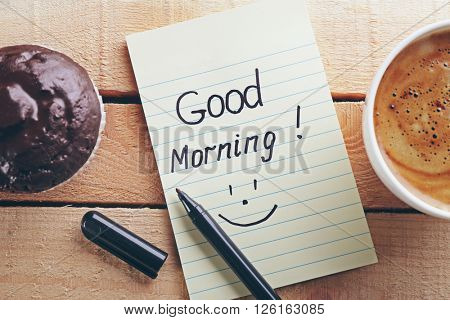 Cup of coffee, chocolate cake and note GOOD MORNING on wooden background