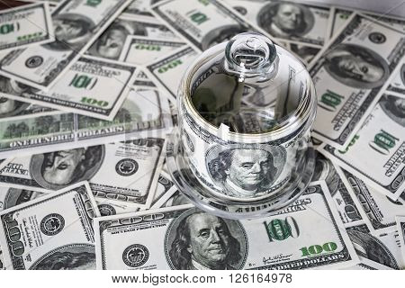 Money in a glass container on the background of one hundred dollar bills. Counterfeit money. Conceptual photo on the business theme. Selective focus.