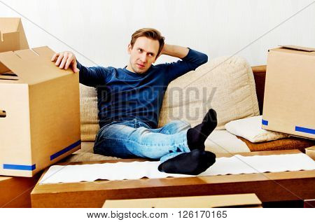 Tired man sitting on couch with cardboard boxes around 
