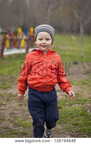 Close up portrait of a beautiful baby boy walking in spring park. Little boy in orange jaket and blue jeans, outdoors