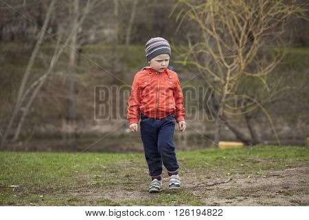 Full length portrait of a beautiful baby boy walking in spring park. Little boy in orange jaket and blue jeans, outdoors