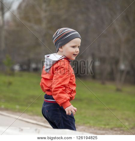 Close up portrait of a beautiful baby boy walking in spring park. Little boy in orange jaket and blue jeans, outdoors