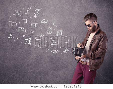 An elegant hipster guy trying to use a vintage camera with camera settings icons drawn on wall, like flash, white balace or ISO value concept