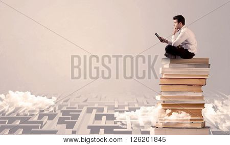 A businessman with laptop tablet in elegant suit sitting on a stack of books on top of sandy labirynth background concept