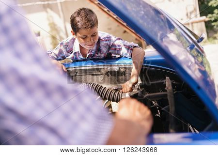 Family and Generation gap. Old grandpa spending time with his grandson. The senior man teaches to the preteen child to fix the engine of a vintage car from the 60s. They smile happy.
