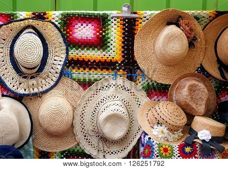 Handmade strawhats with colorful ribbons are displayed by an outdoor vendor
