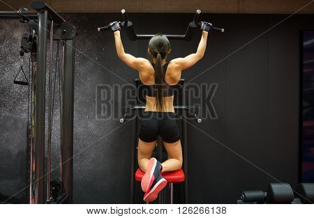 sport, fitness, lifestyle and people concept - woman exercising and doing pull-ups in gym from back