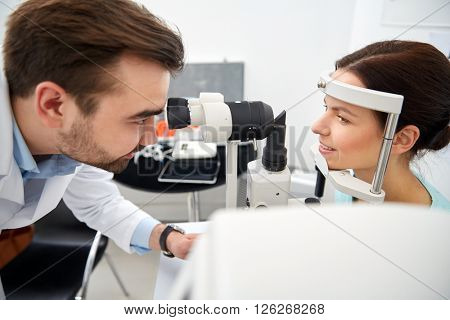 health care, medicine, people, eyesight and technology concept - optometrist with non contact tonometer checking patient intraocular pressure at eye clinic or optics store